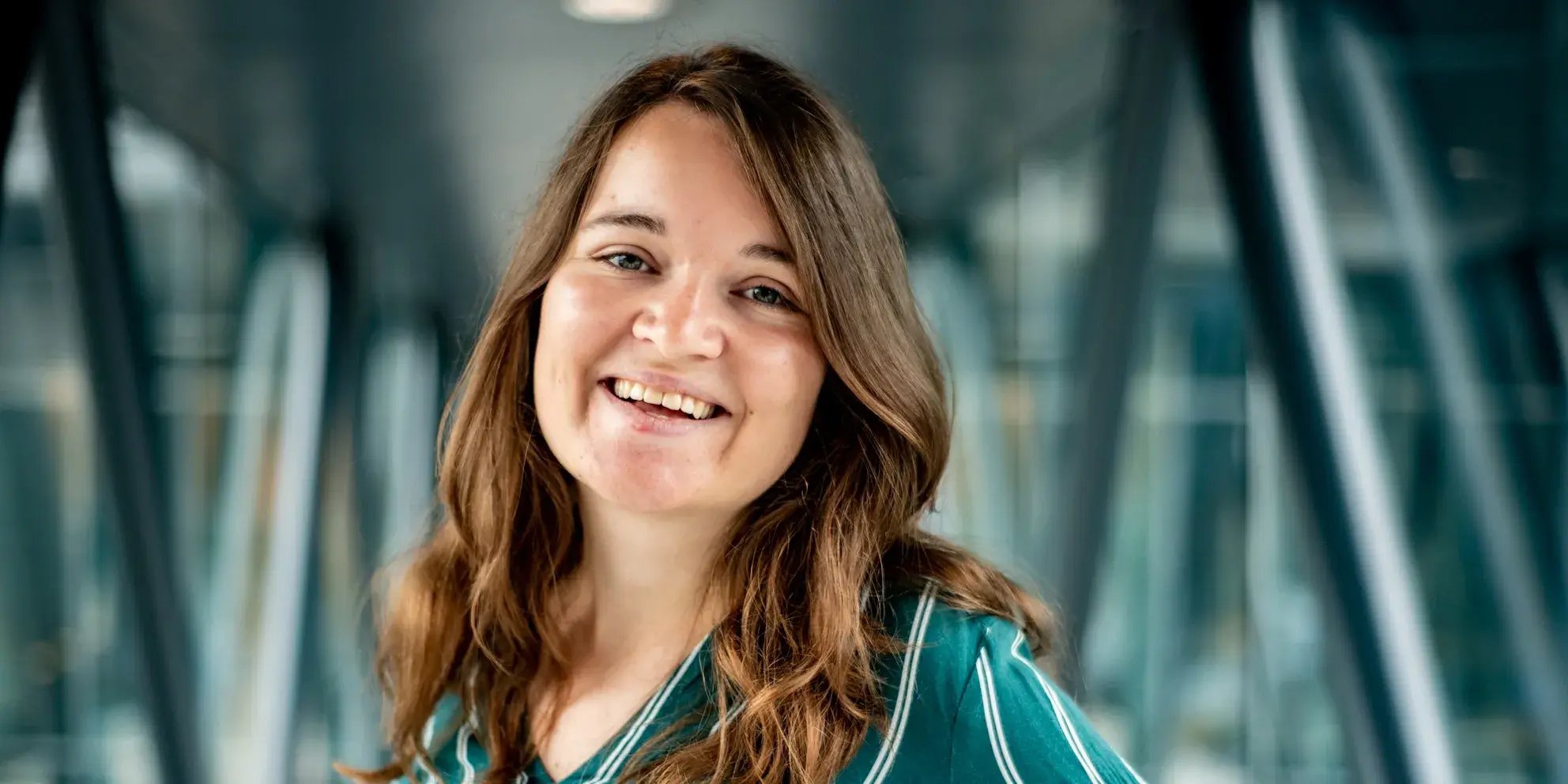Lachende vrouw met lang bruin haar in groene blouse in moderne gang.