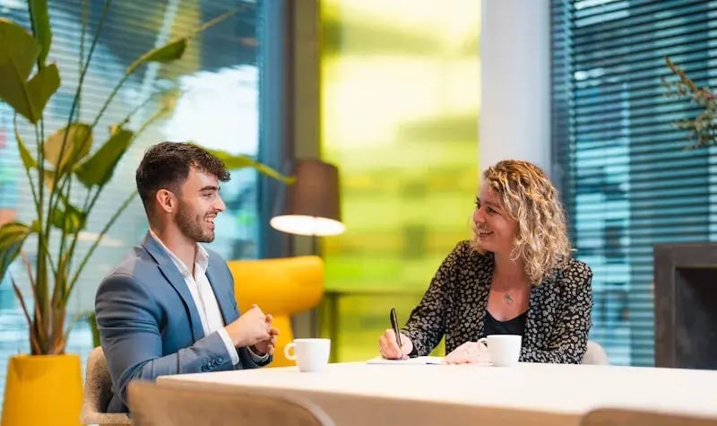 Man en vrouw aan tafel met kop koffie en lachen naar elkaar