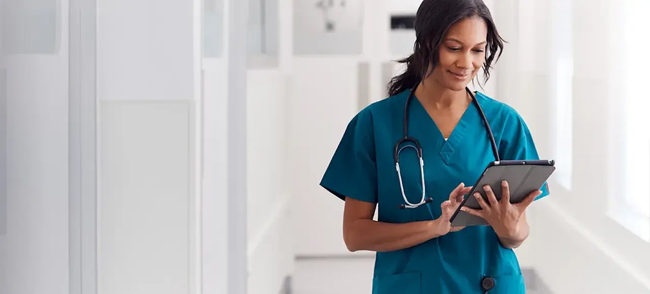 Vrouw in de zorg met telescoop om haar nek en tablet in haar handen.