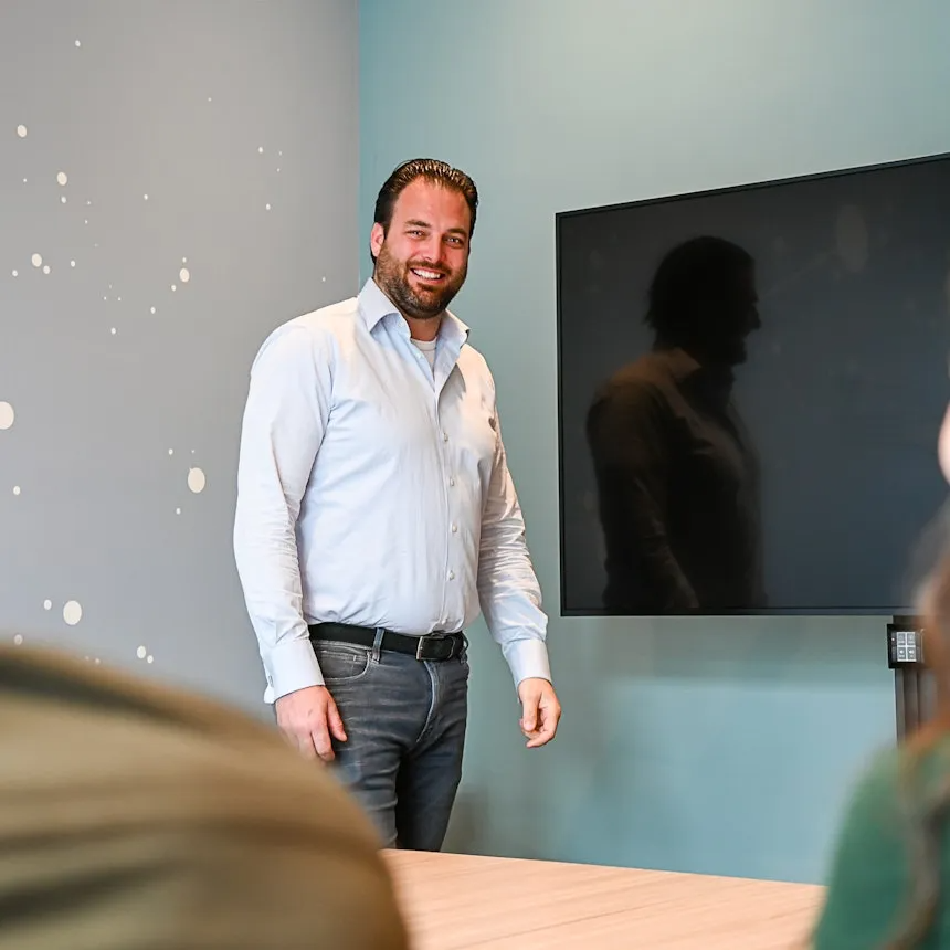 Man in lichte blouse naast tv scherm