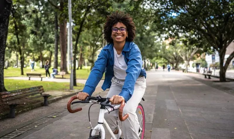 Vrouw met kroeshaar op de fiets lachend richting de camera