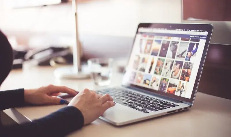 Laptop op een bureau met afbeeldingen op het scherm en twee handen van een vrouw. 