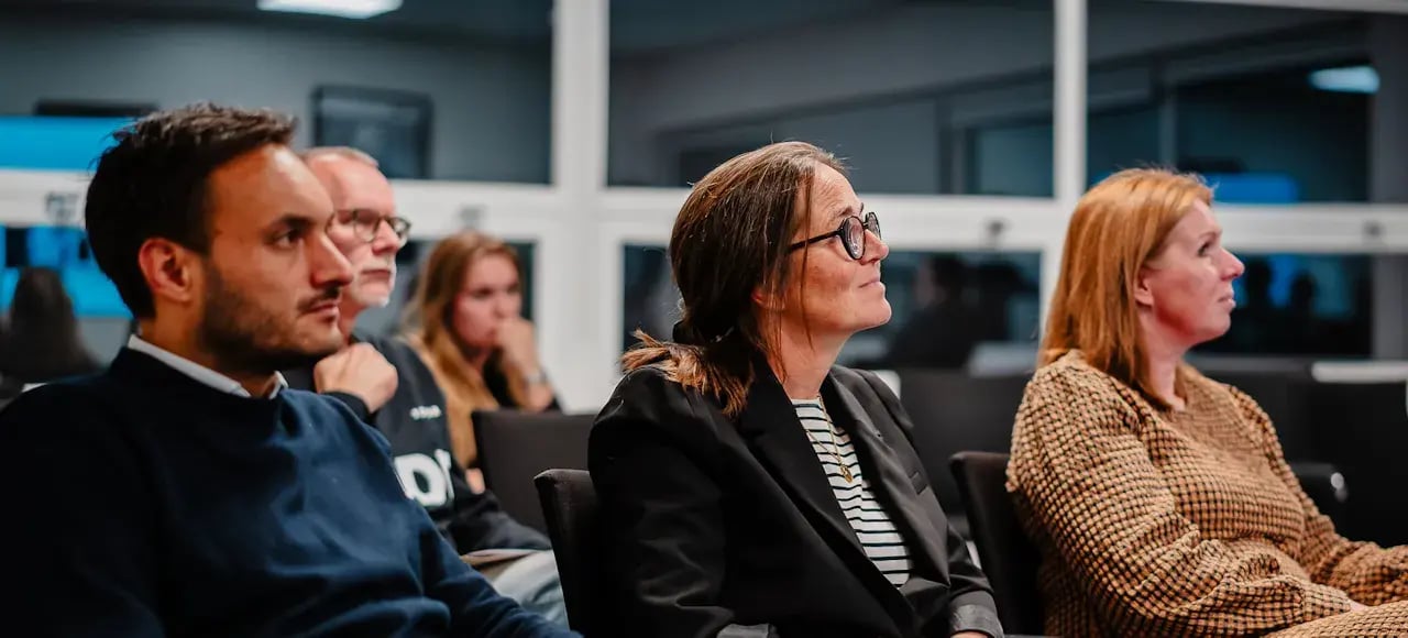 Collega's naast elkaar zittend op een stoel die luisteren naar iemand die en presentatie geeft