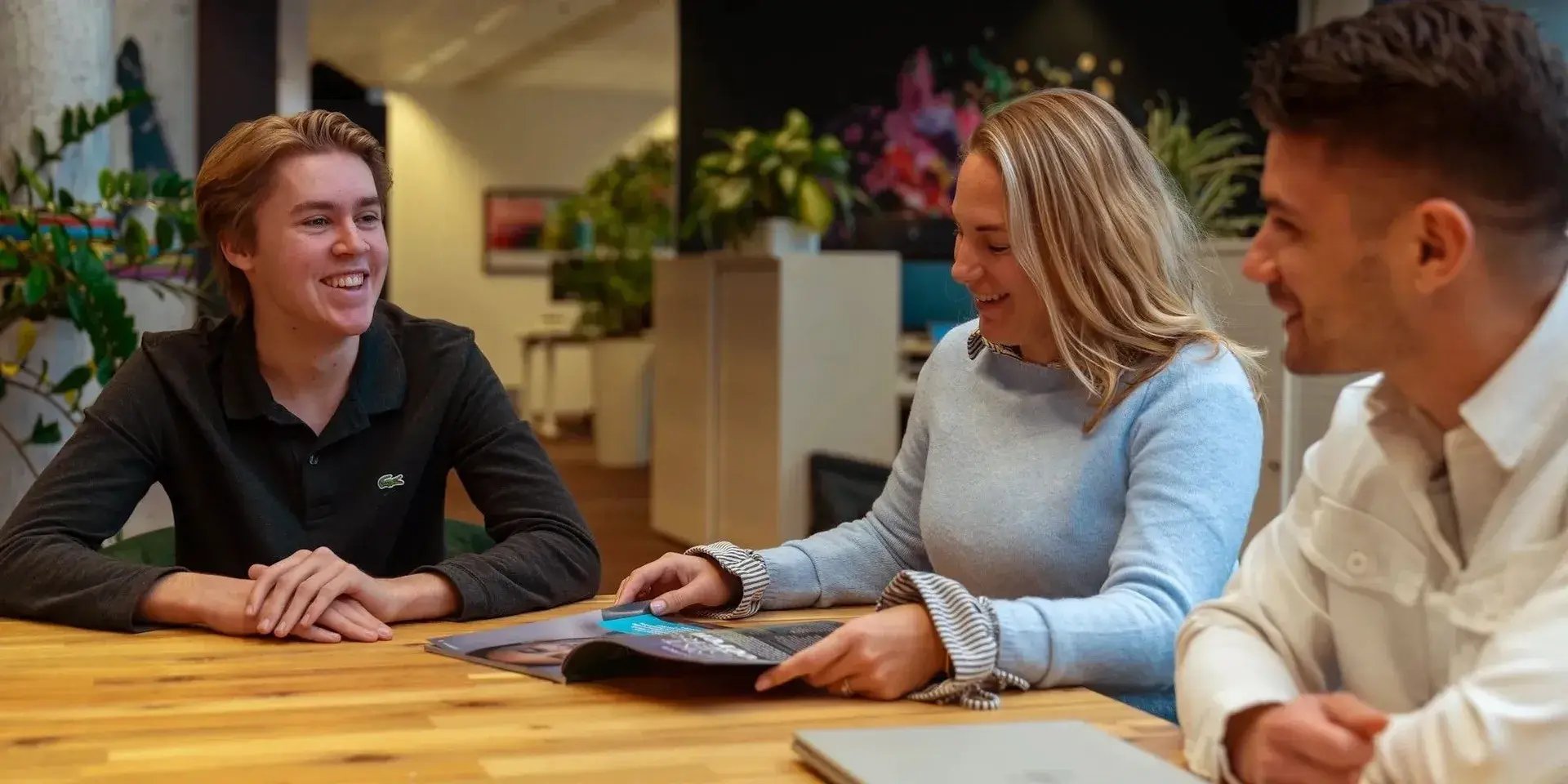 Twee mannen en een vrouw lachen tijdens een informeel overleg aan tafel.