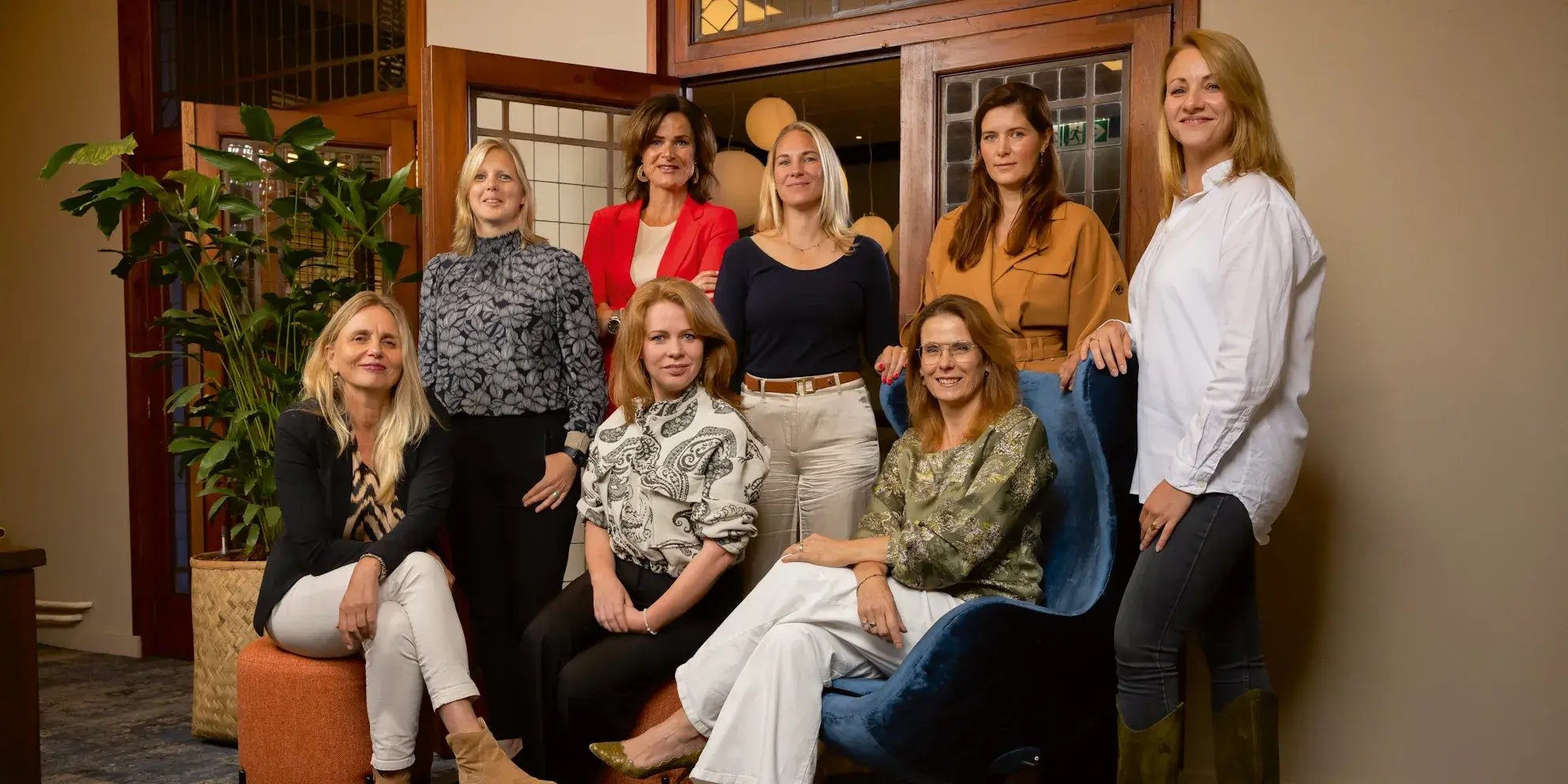 Groepsfoto van acht vrouwen samen in een kantoorruimte.