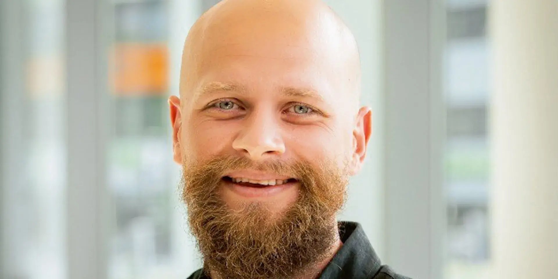 Close-up portret van een lachende man met een kale hoofd en volle baard.