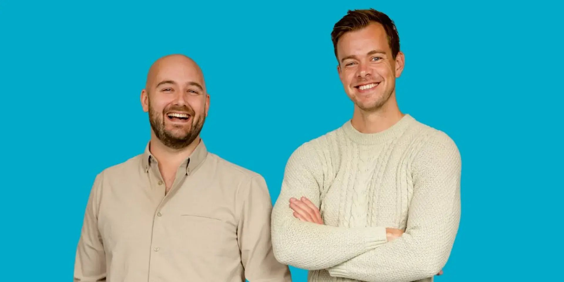Twee lachende mannen staan naast elkaar voor een effen blauwe achtergrond.