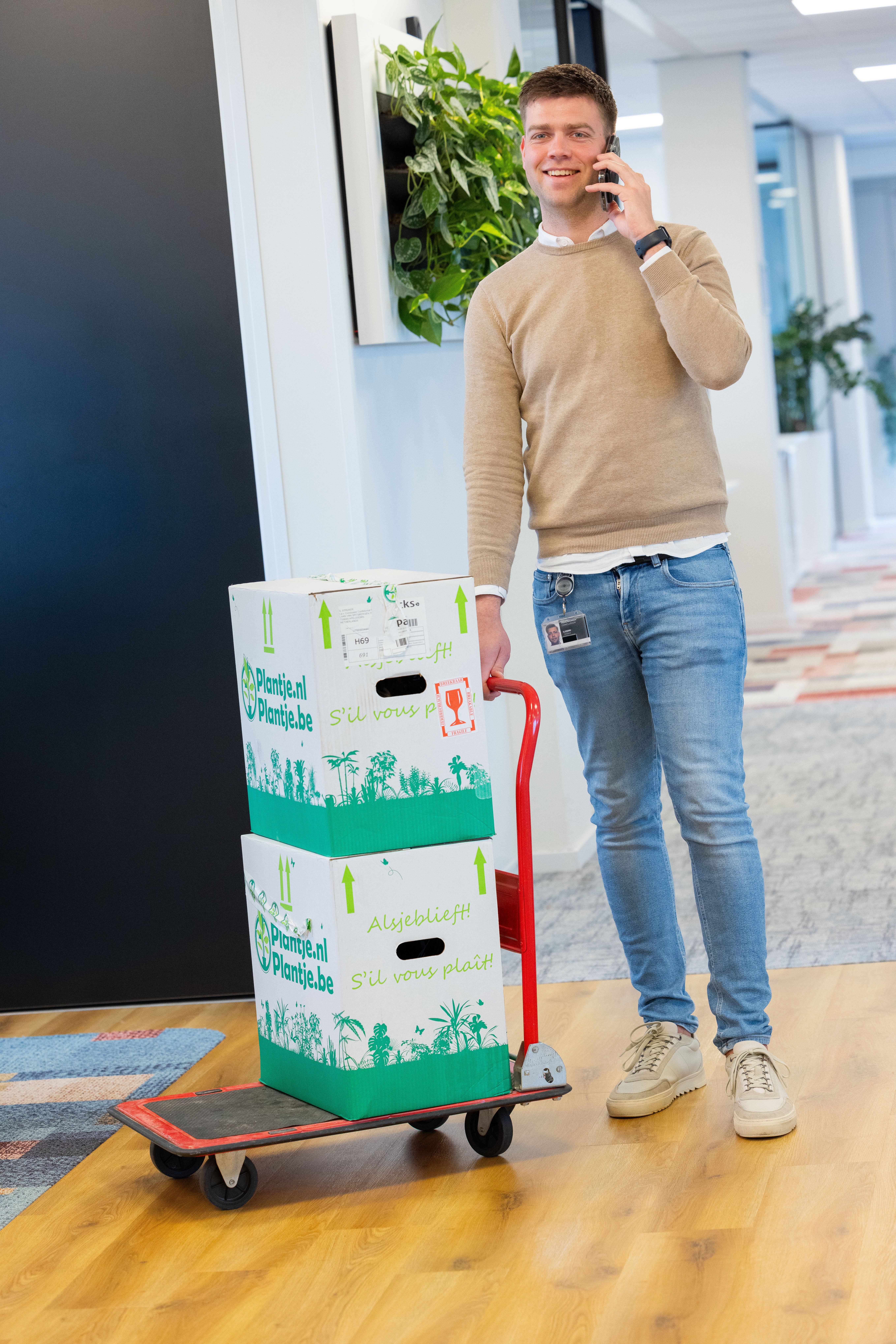 Man loopt met plantendozen door het kantoor en pleeg een belletje.