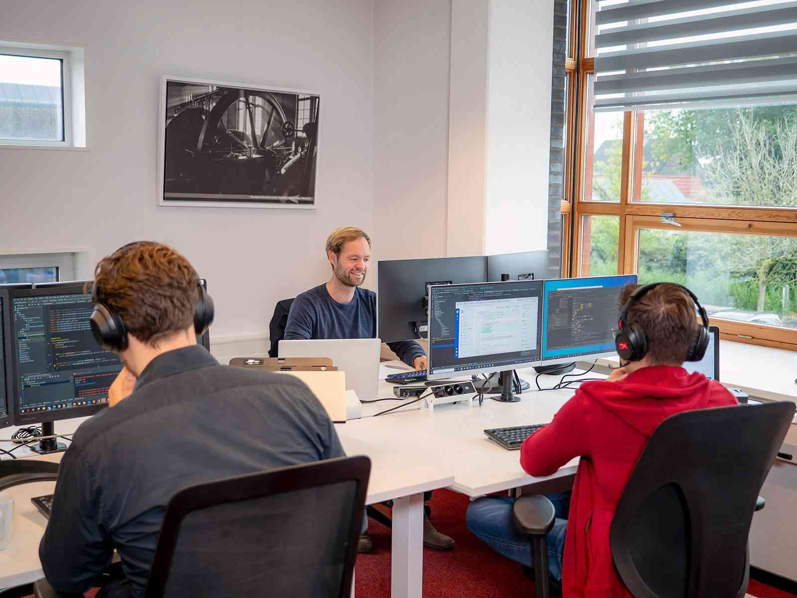 Twee mensen werken geconcentreerd achter meerdere monitoren in een kantoor.