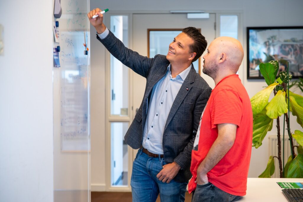 Twee mannelijke collega's schrijven op een whiteboard.