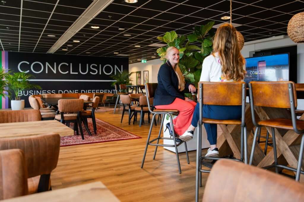 Twee vrouwen zitten op hoge stoelen en kletsen met elkaar.