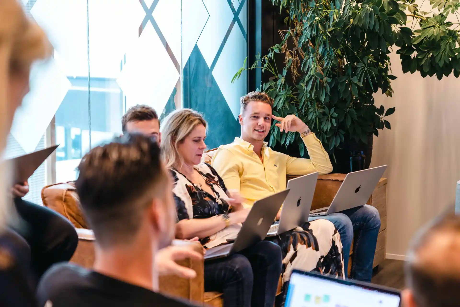 Een groep collega's bij elkaar in een ruimte zittend op bank met laptops op schoot.