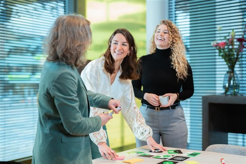 Drie vrouwen lachen en werken met kaarten in een kantoor.