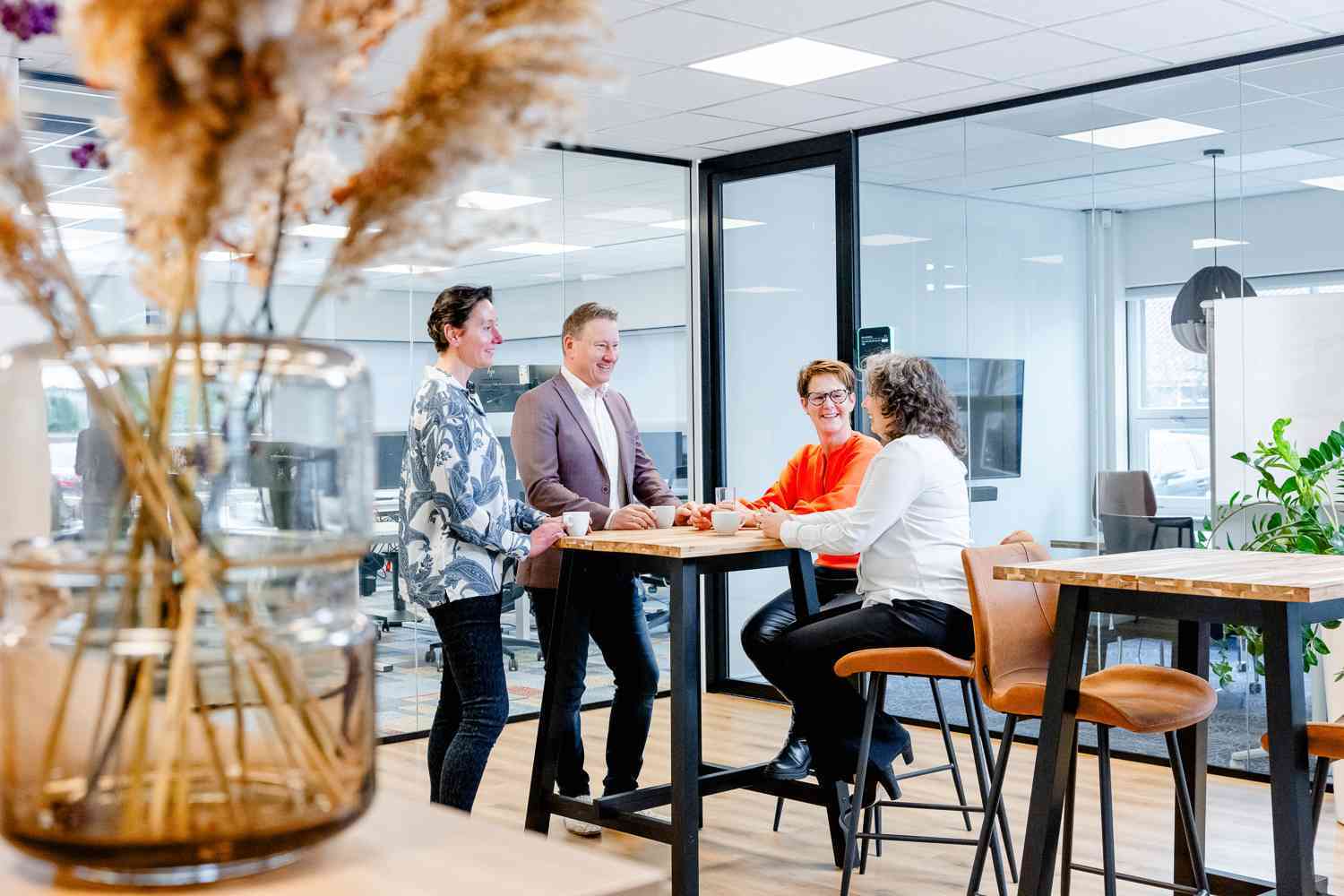 Vier collega's zitten aan een hoge tafel en kletsen met elkaar.