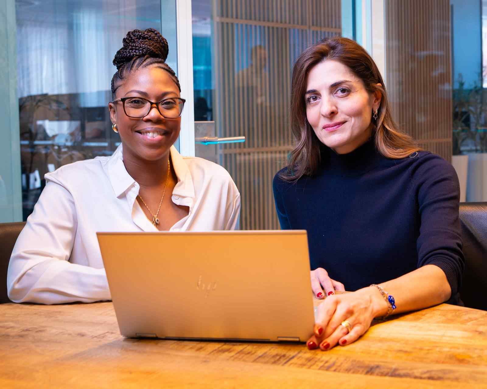 Twee vrouwen werken samen aan een laptop in een vergaderruimte.