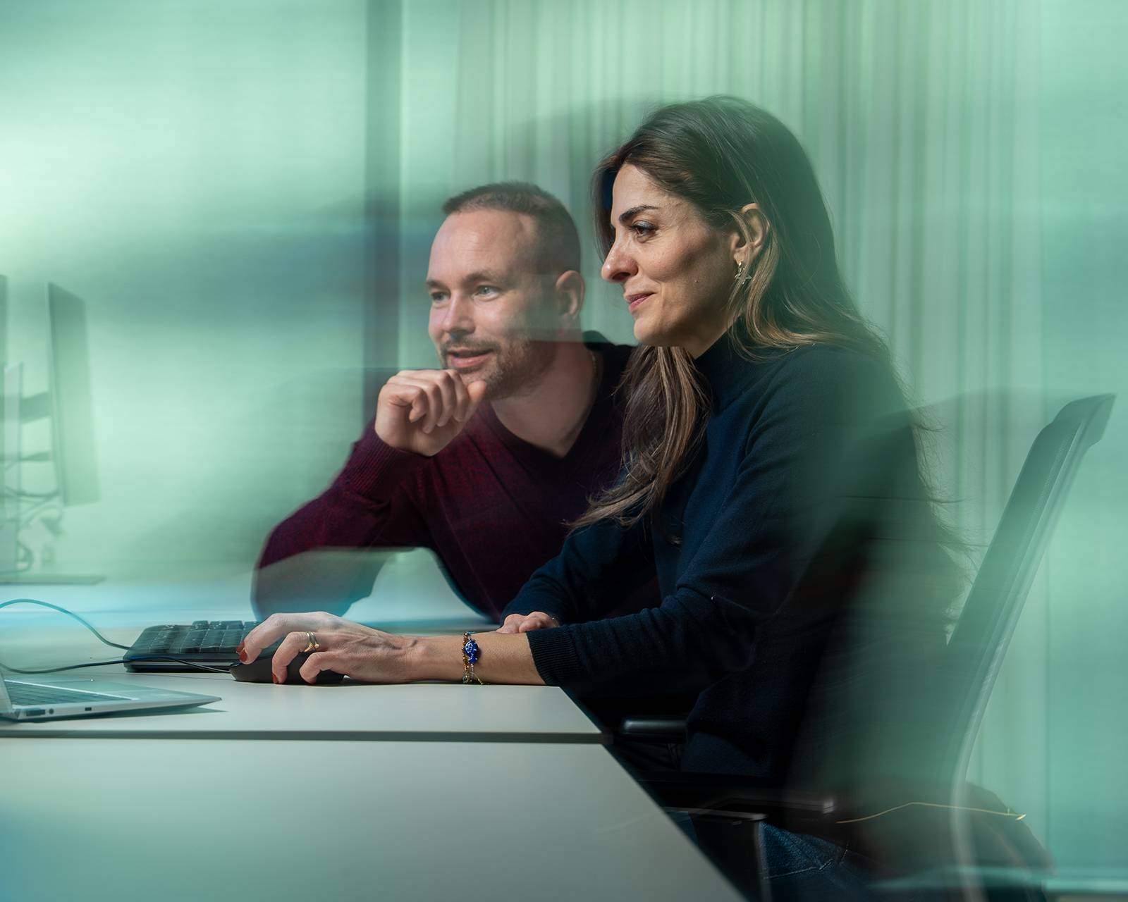 Twee collega's werken samen aan een computer, met de focus op het scherm.