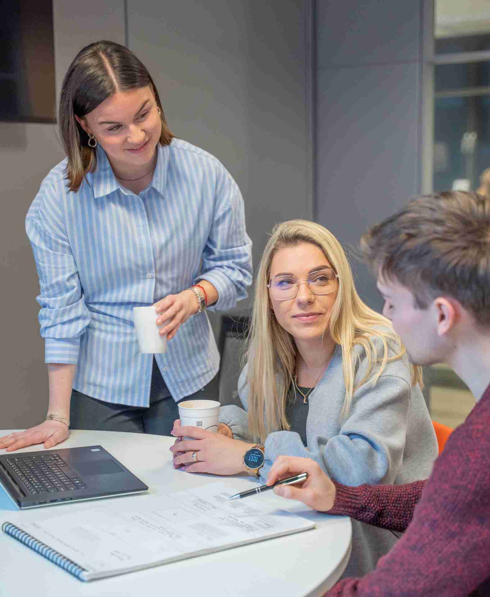 Twee collega's overleggen aan een bureau en een andere collega staat er nog bij en leunt op de tafel.