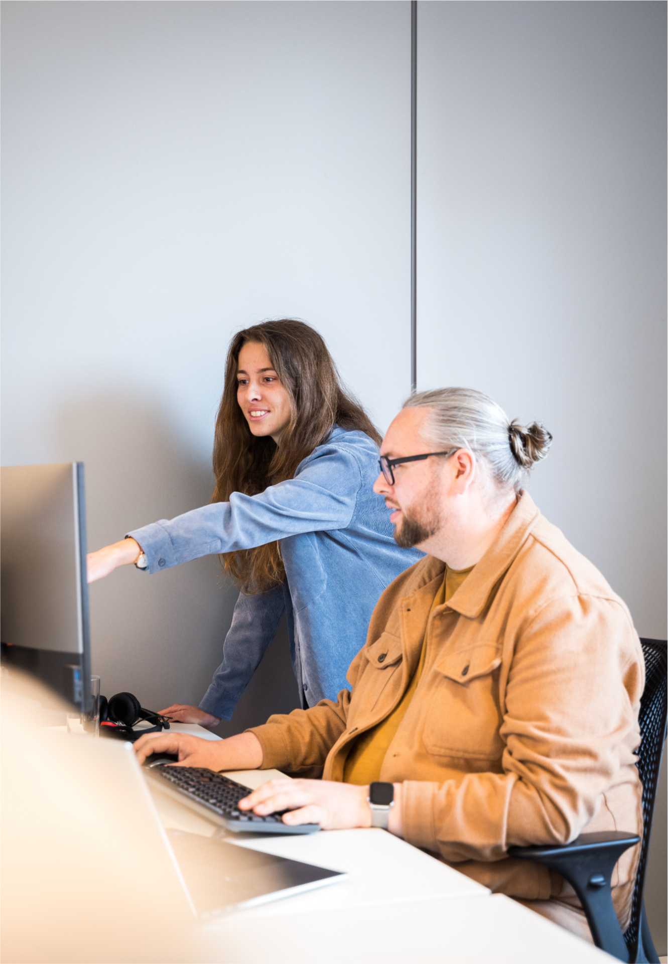 Een vrouwelijke collega wijst vriendelijk naar het scherm van een man.