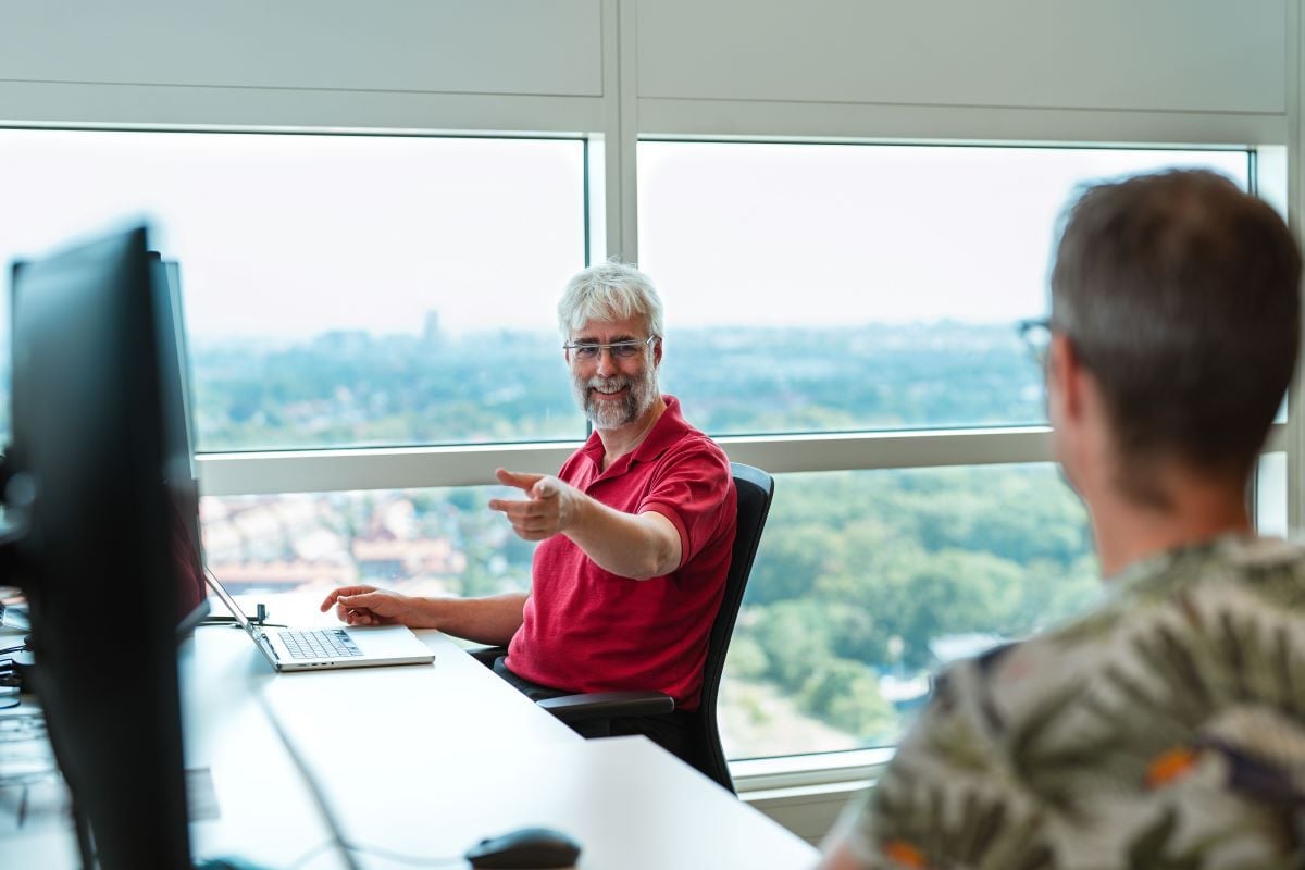 Een man wijst terwijl hij achter zijn bureau zit, met uitzicht over de stad.