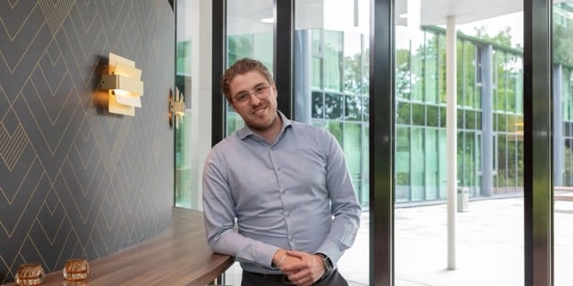 Man leunt op een tafel en lacht voor zich uit.