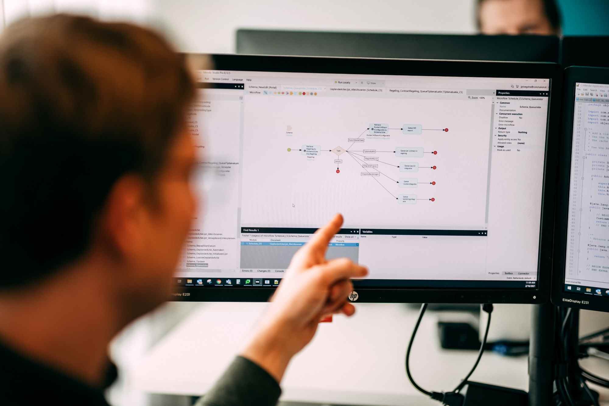 Man wijst naar een scherm met een visuele weergave van code en processen.