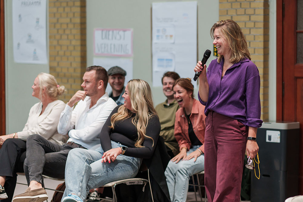Een vrouw presenteert vrolijk voor een groep collega's.