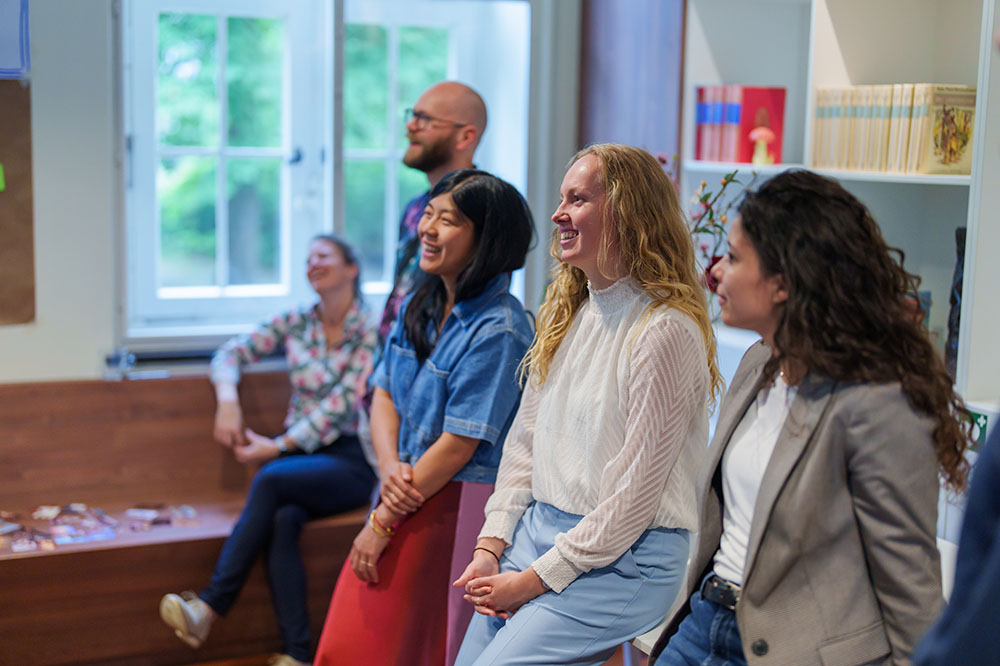 Vijf mensen lachen samen in een kamer.