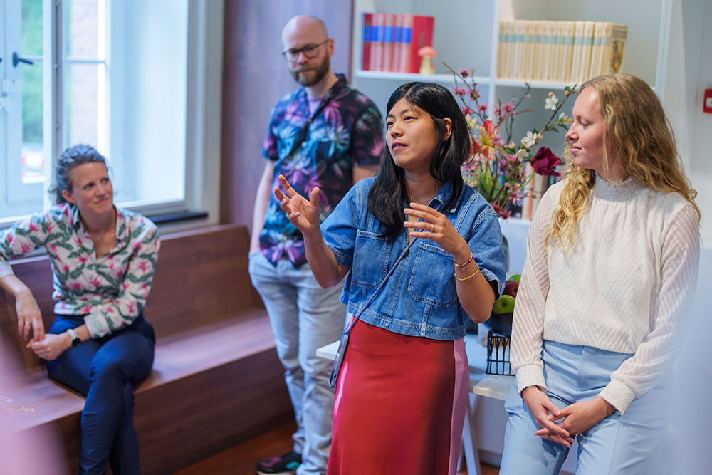 Een vrouw geeft een presentatie terwijl anderen aandachtig luisteren.