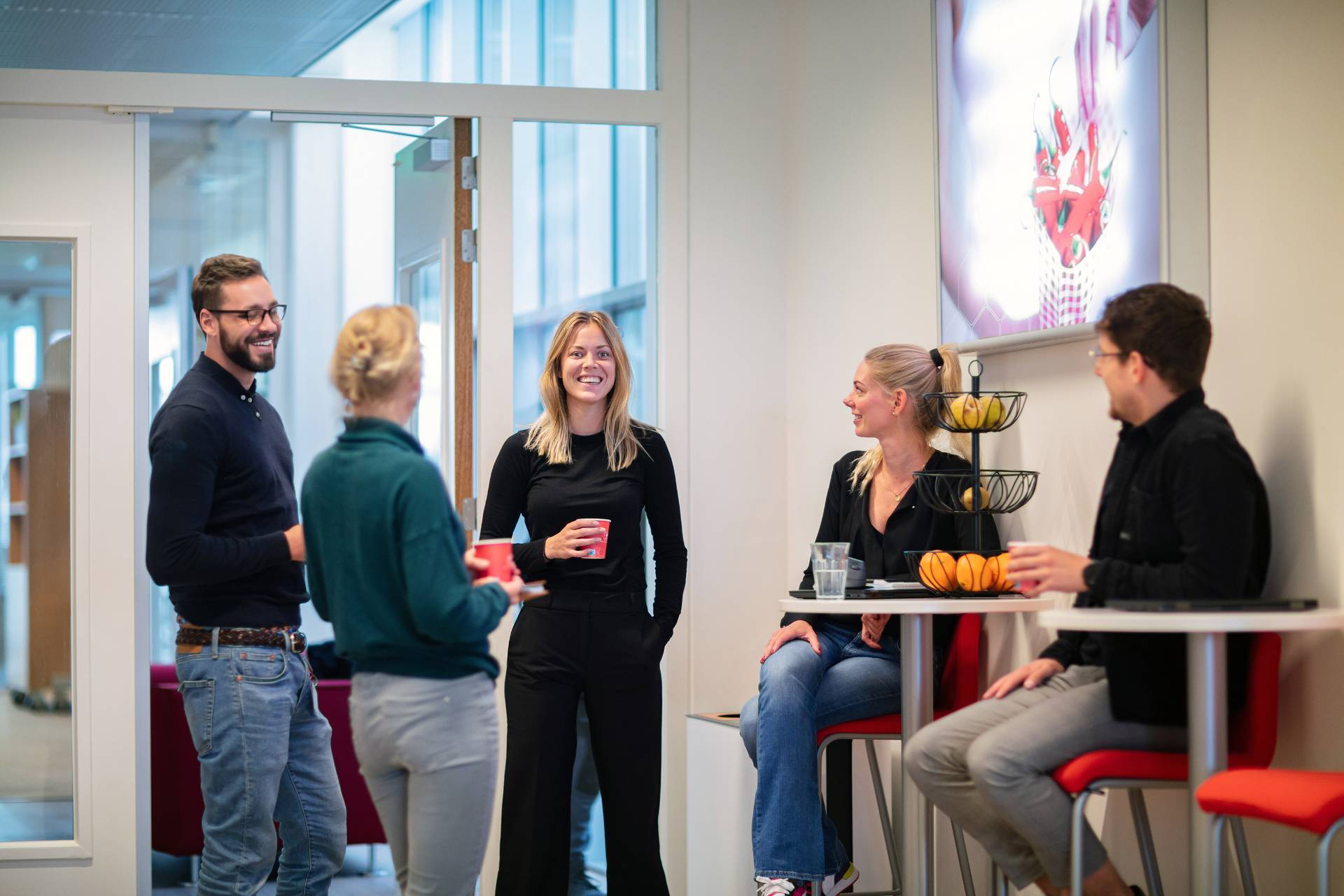 Vrouw lacht naar voren en staat in een groep van collegas met koffie.