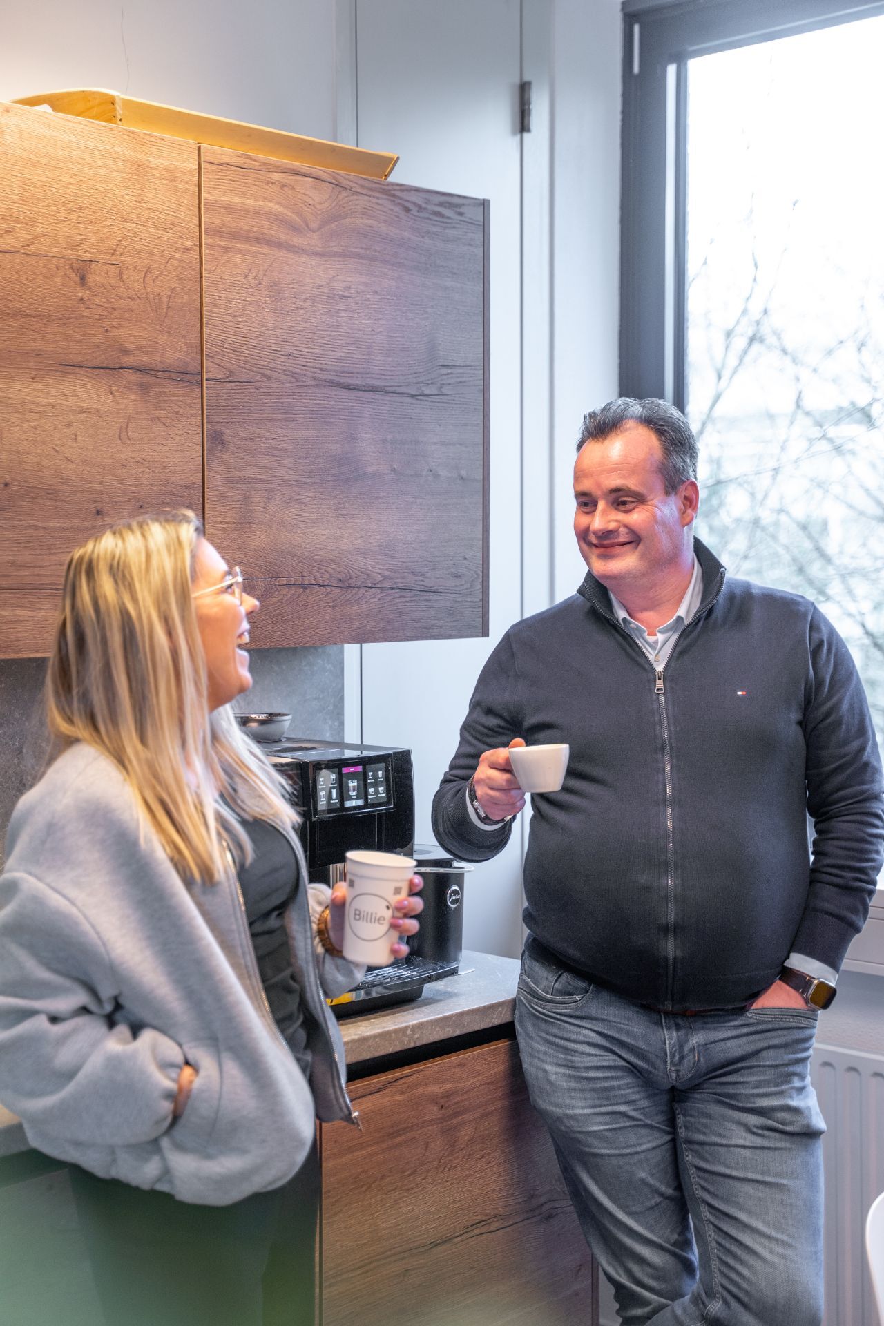 Man en vrouw kletsen bij een koffiezetautomaat.