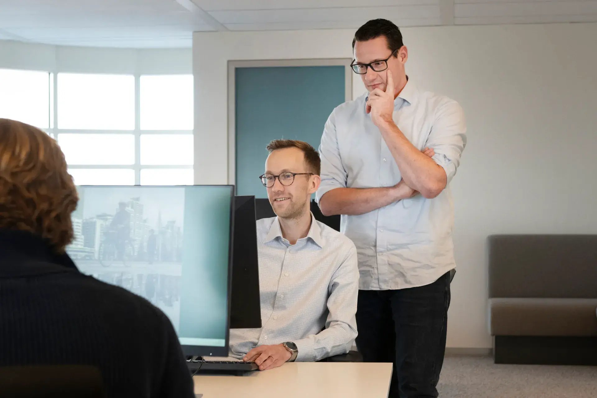 Man zittend achter laptop en andere man staand kijken samen naar scherm.