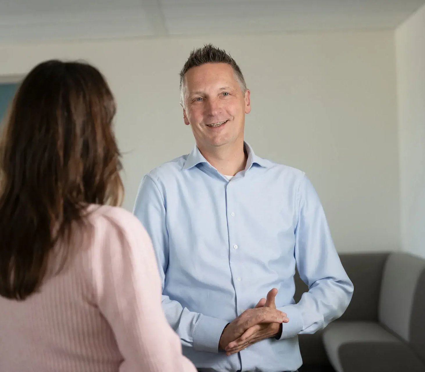 Man in blauw overhemd in gesprek met vrouw met donker lang haar.