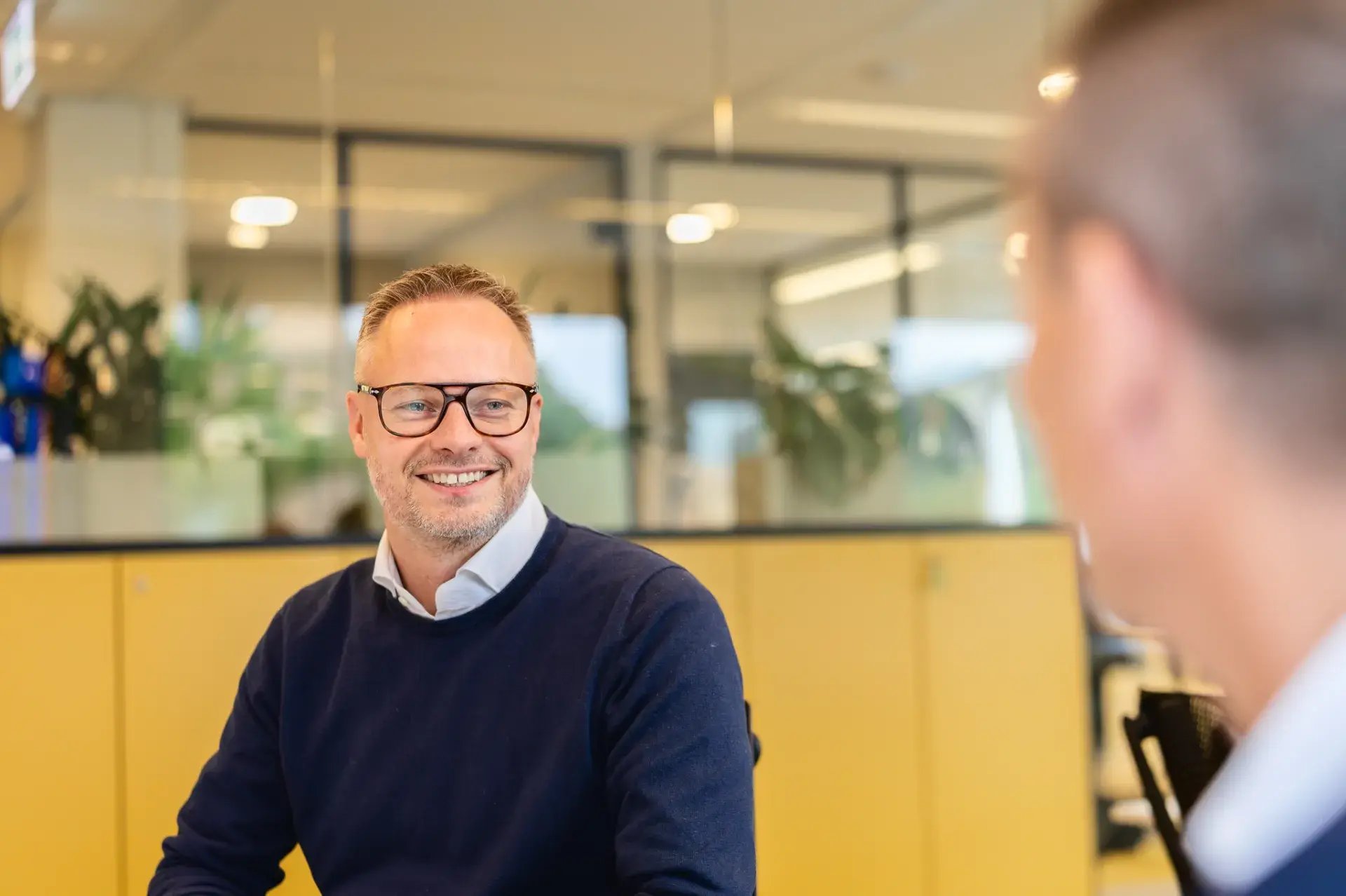 Man wearing glasses talking to another man.