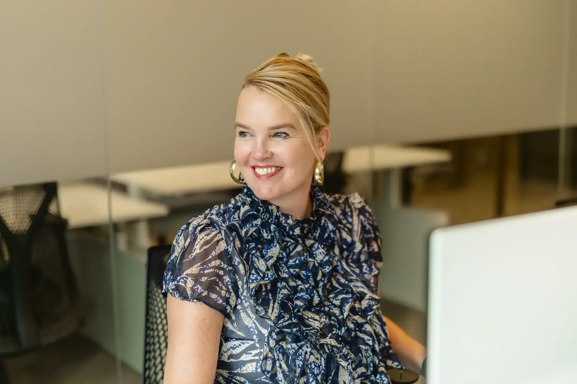 Blonde woman with her hair up behind a laptop.