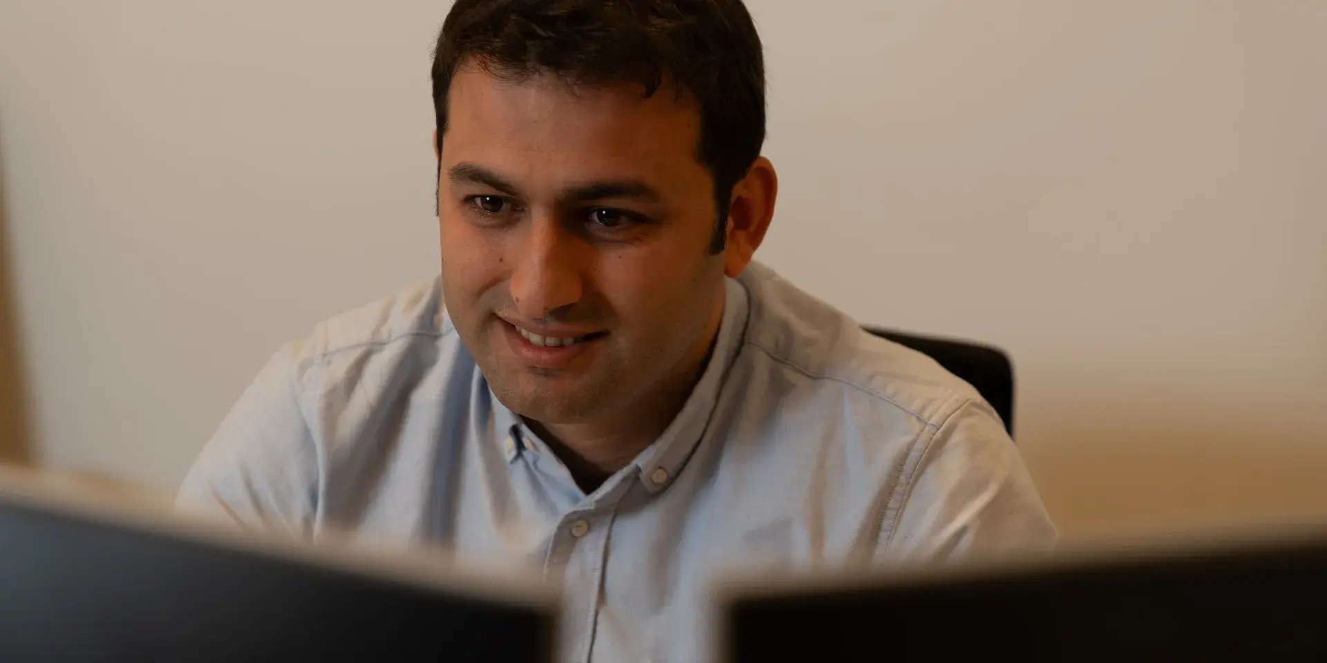 Man glimlacht terwijl hij achter twee computerschermen werkt.