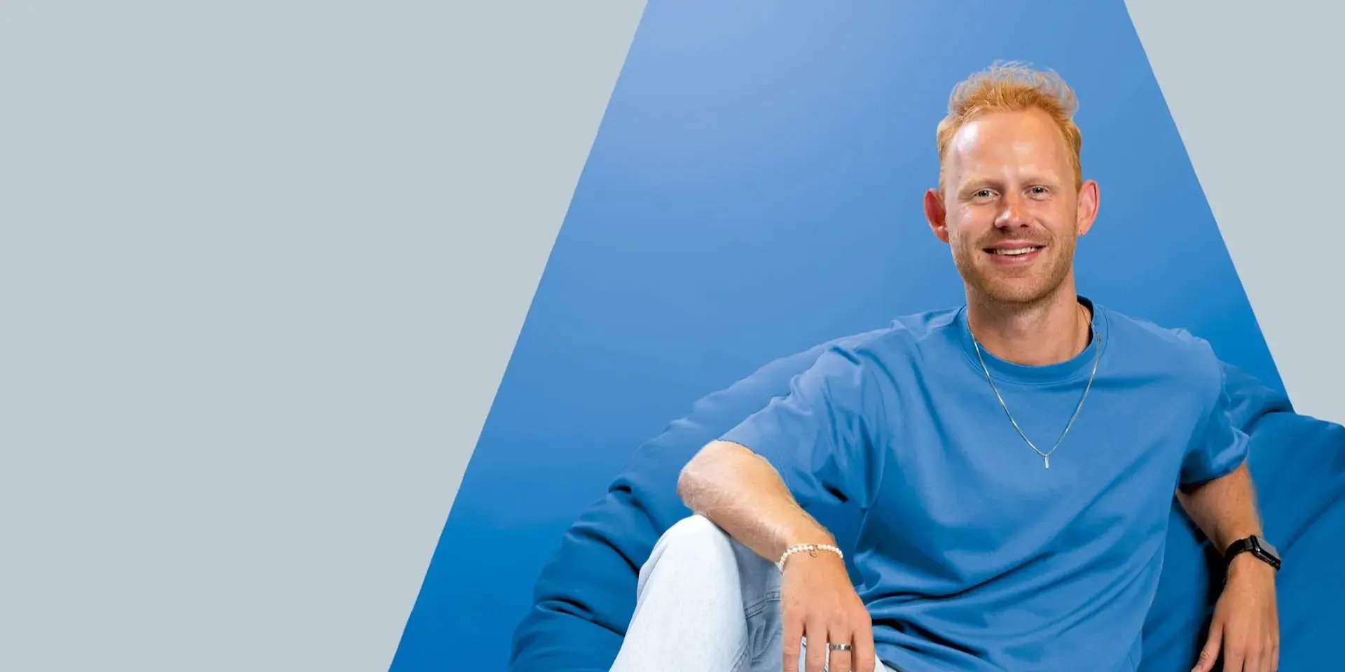 Man in blauwe outfit zit lachend tegen een blauwe achtergrond.