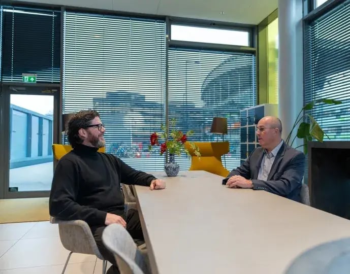 Two male colleagues in conversation at long table.