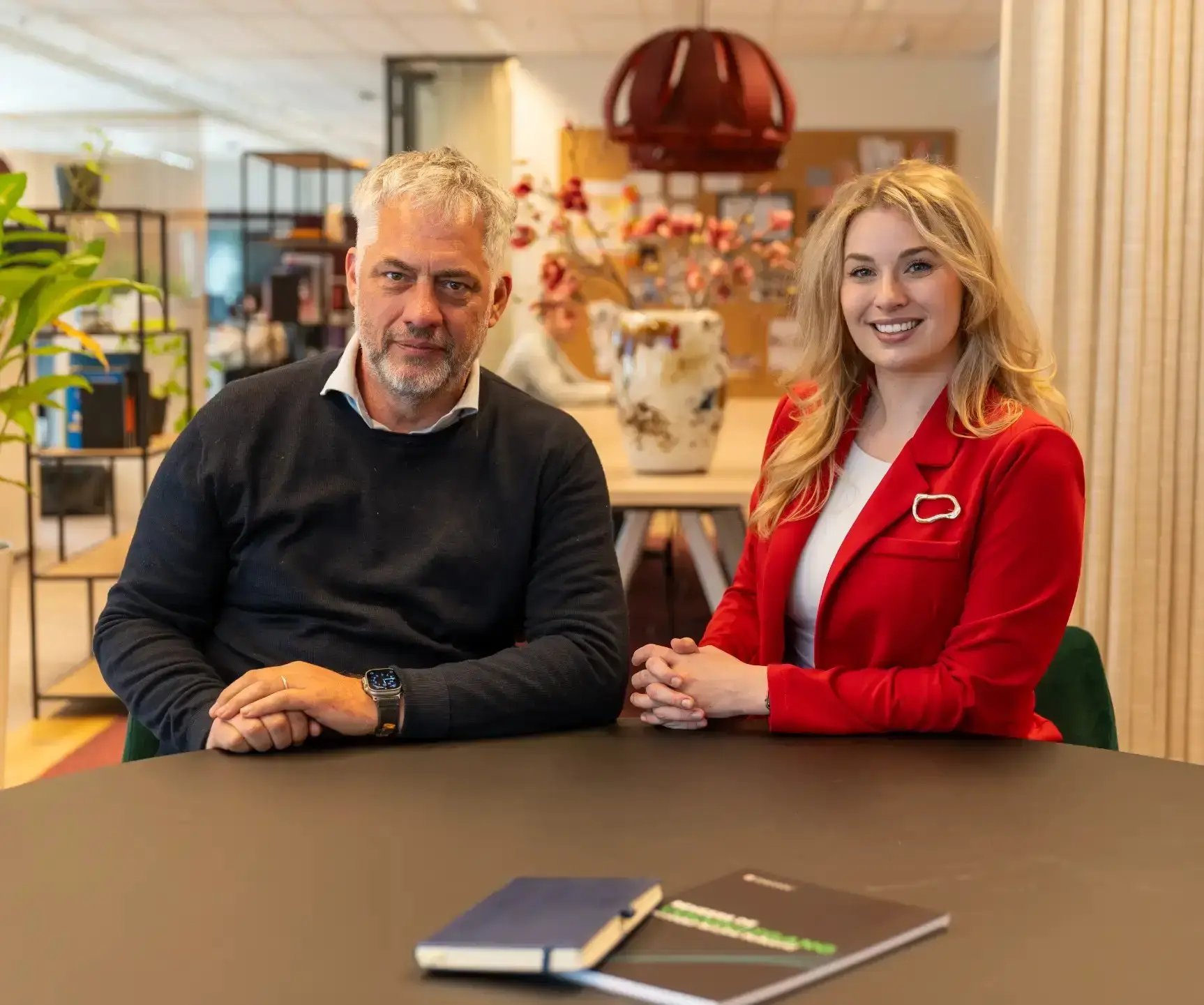 Man met grijs haar en baard en vrouw met lang blond haar zitten aan tafel.