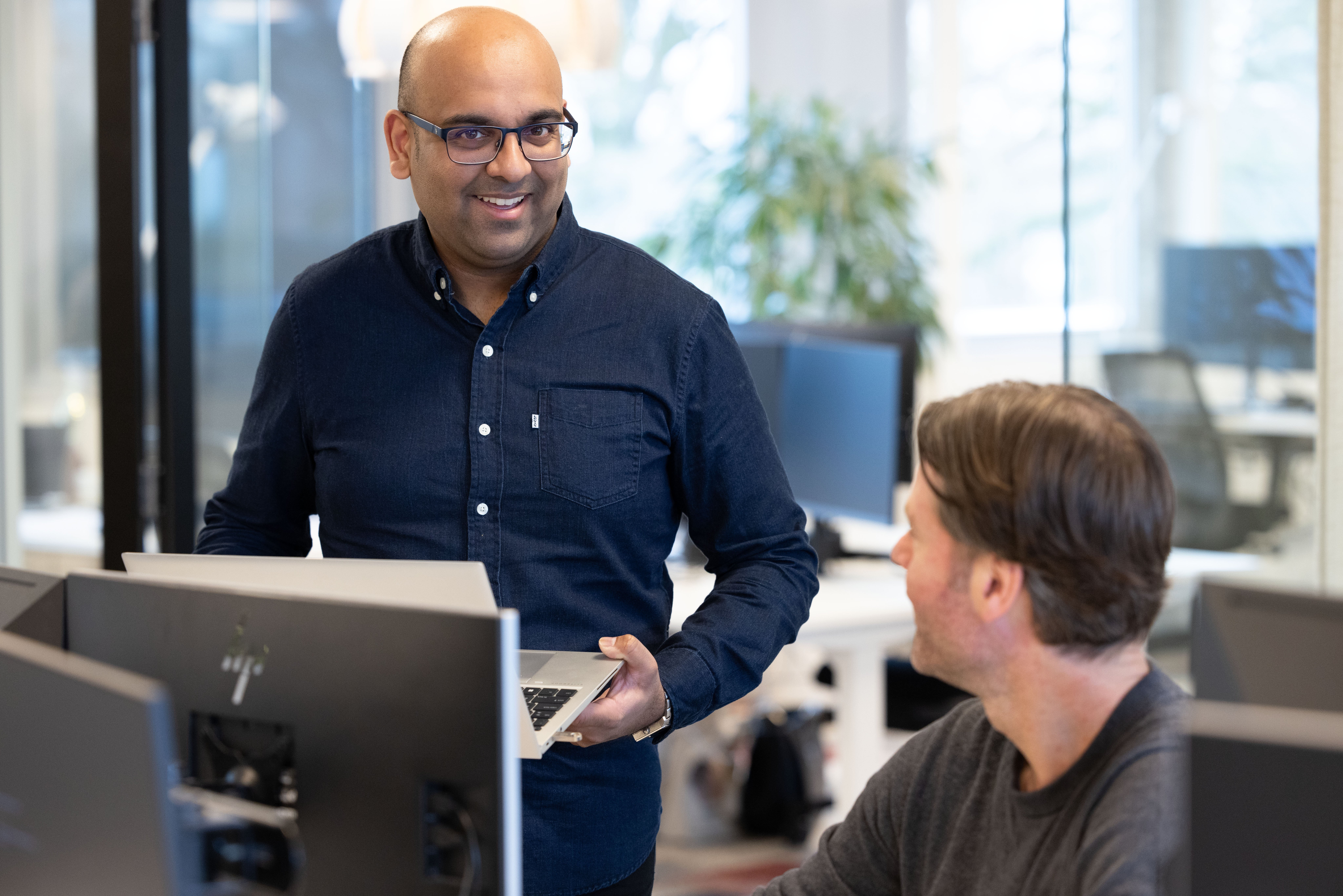 Twee mannelijke collega's achter computer scherm lachen naar elkaar