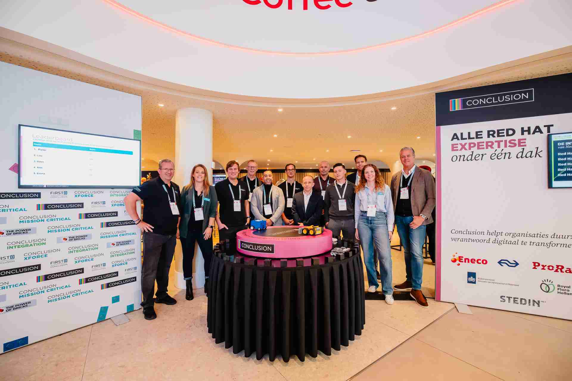 Groep mensen poseert bij een tafel op een beurs.