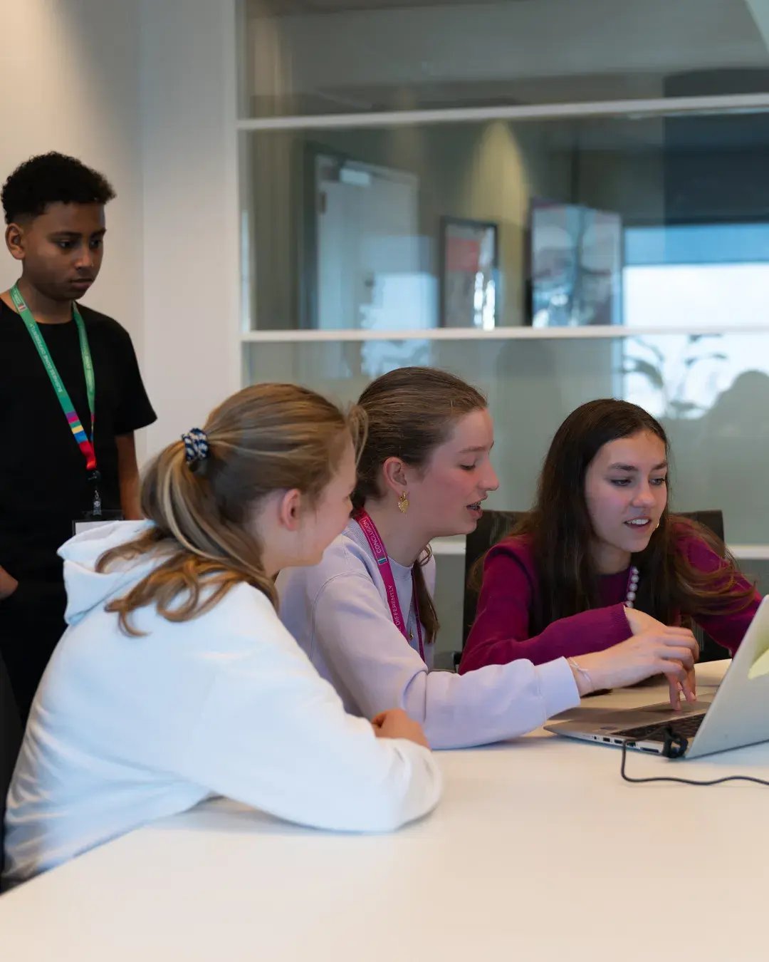 Drie meiden achter laptop en een jongen die kijkt wat ze doen.