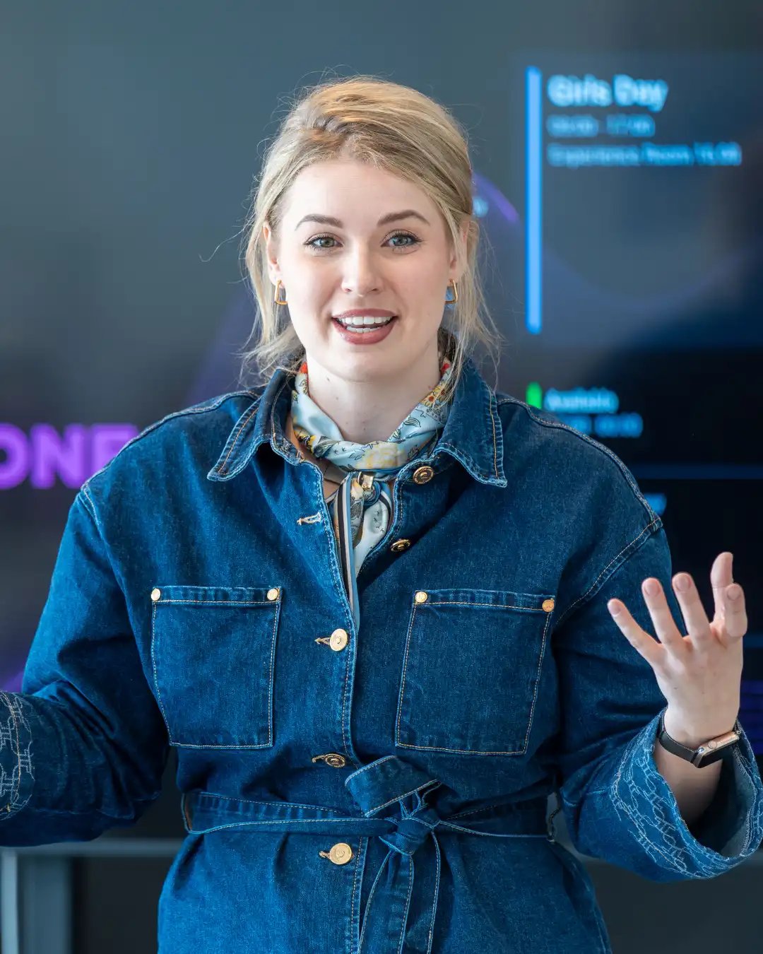 Vrouw met blond opgestoken haar in spijkerpak.