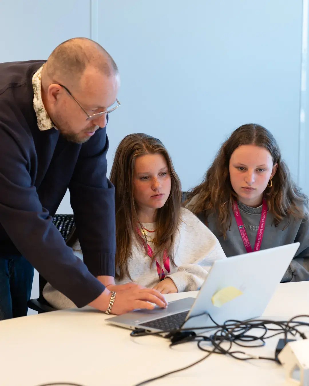 Man legt iets uit aan 2 meiden bij laptop.