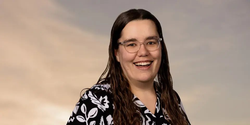 Woman with long dark hair and glasses smiles at the camera.