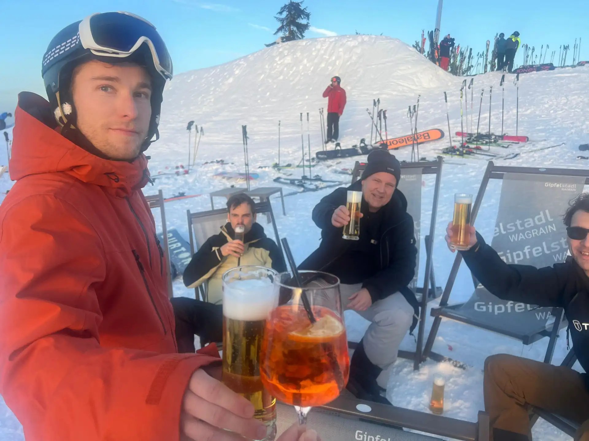 Man in a red ski jacket holding a beer at a bar on the slope.
