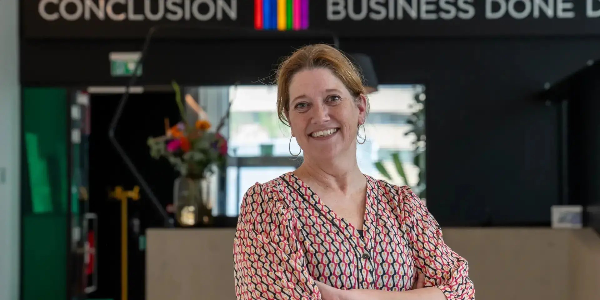 Lachende vrouw met armen over elkaar kijkt in camera.