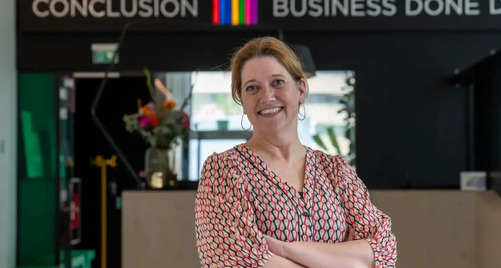 Lachende vrouw met armen over elkaar kijkt in camera.