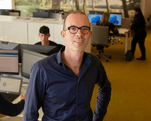 Personeelslid in een open kantooromgeving met laptops en bureaus.