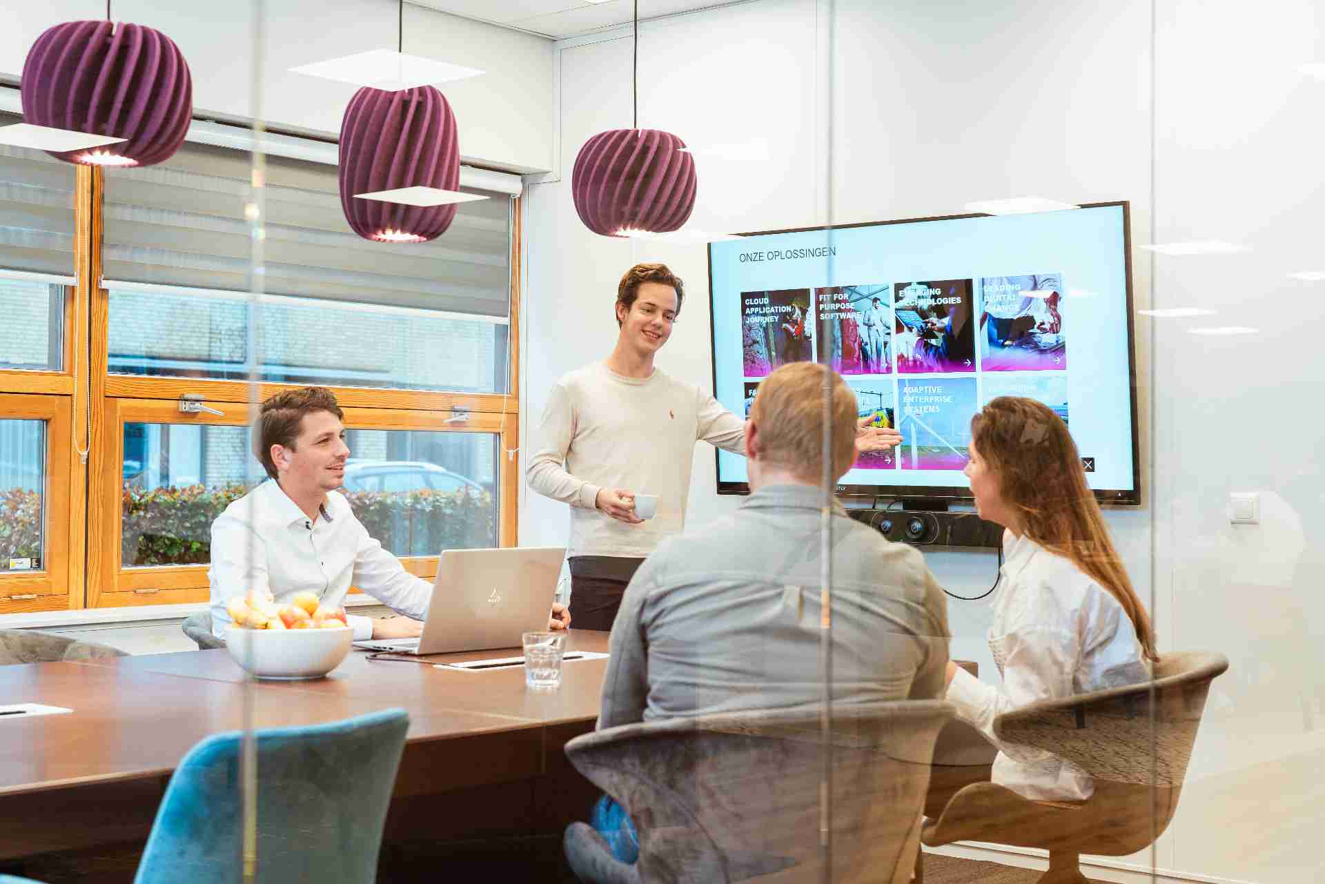 Een man presenteert aan drie collega's in een vergaderruimte.