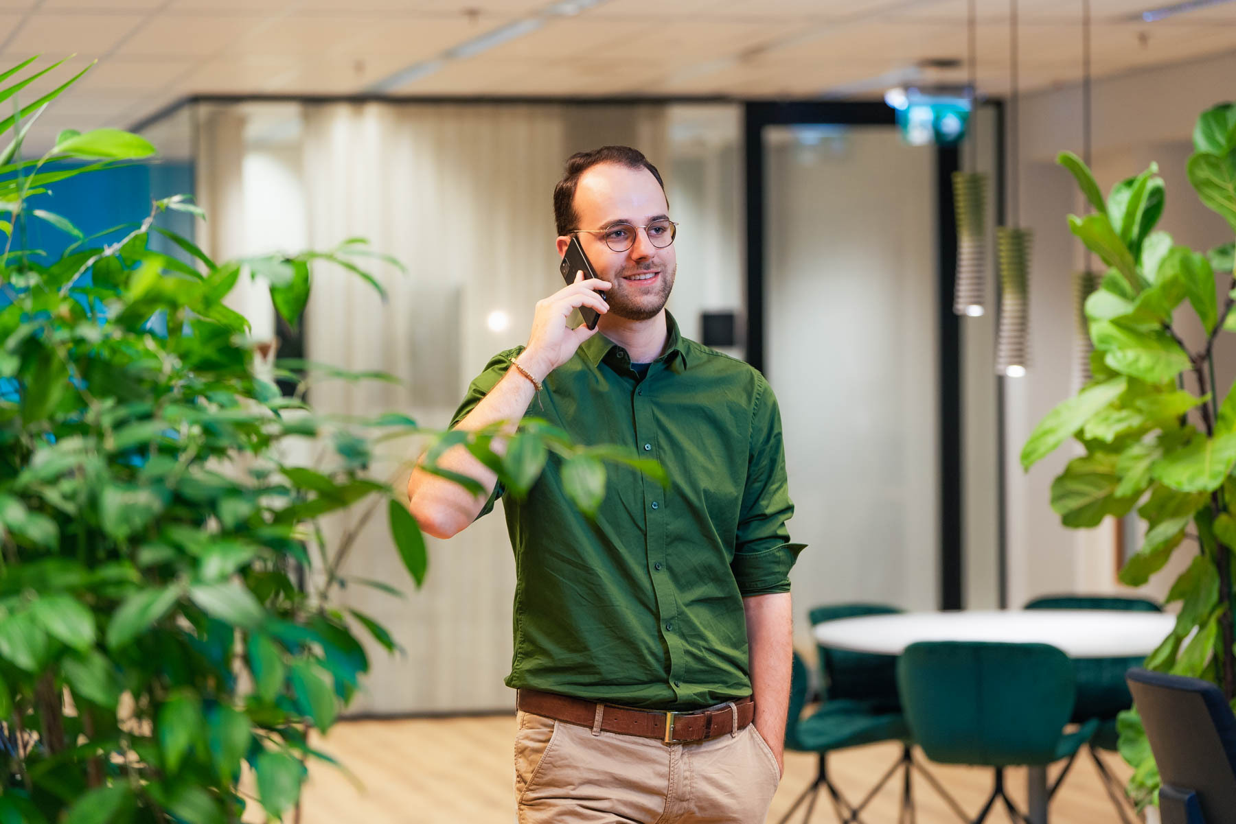 Man telefoneert in een modern kantoor met veel groen.